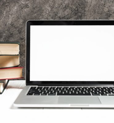 red-apple-stacked-books-near-laptop-white-desk-against-concrete-wall_23-2148041884